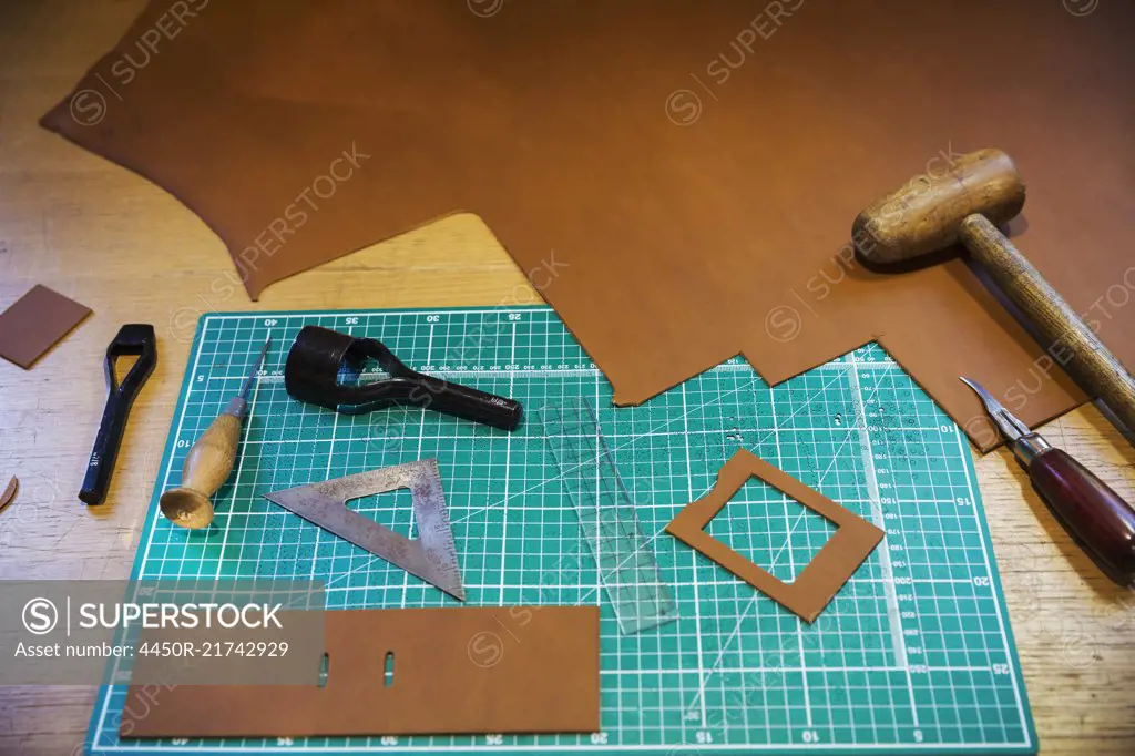 Workbench and cutting mat with a large smooth piece of brown leather, and  tools for measuring cutting and stitching, leatherworking tools. -  SuperStock