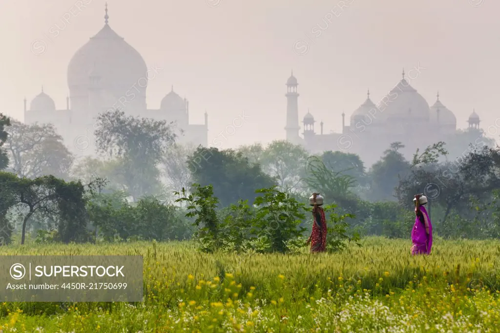 Exterior view of the Taj Mahal in Agra, India. Two woman in the foreground carrying loads on their heads.