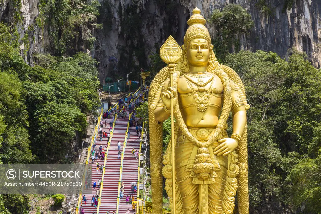 Colossal golden statue of Hindu deity, with stairway into cave in the background.