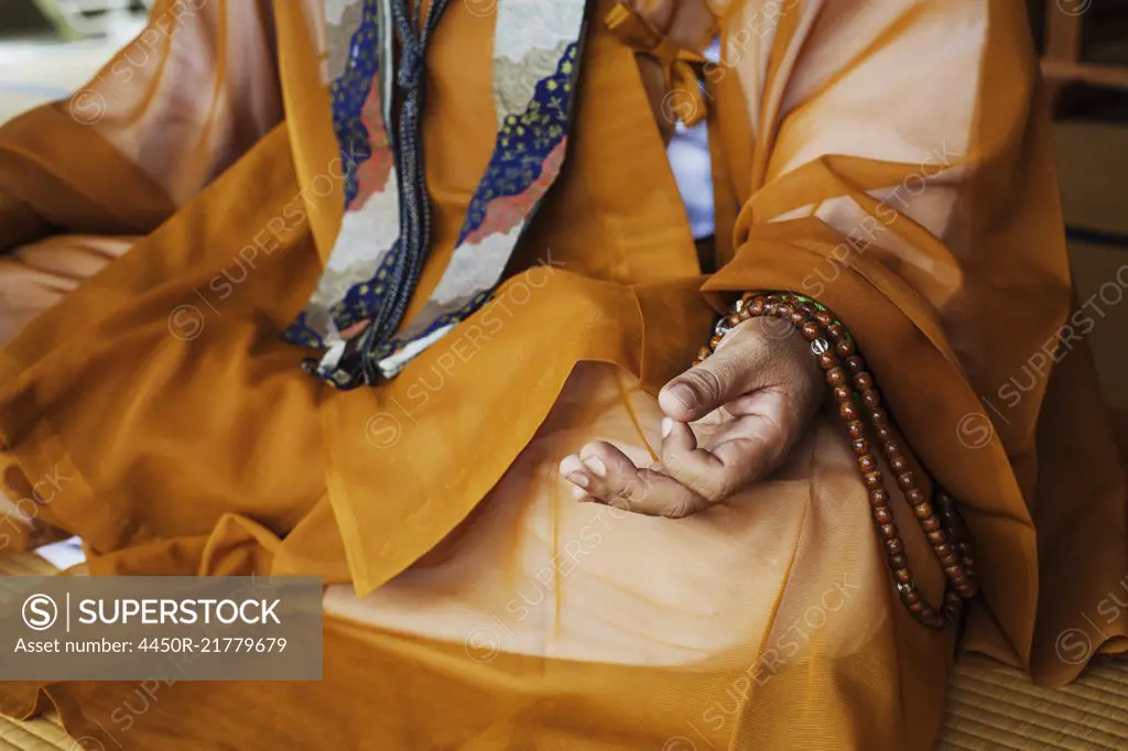 Close up of Buddhist monk wearing golden robe sitting cross legged on the floor, meditating, Buddhist hand gesture.