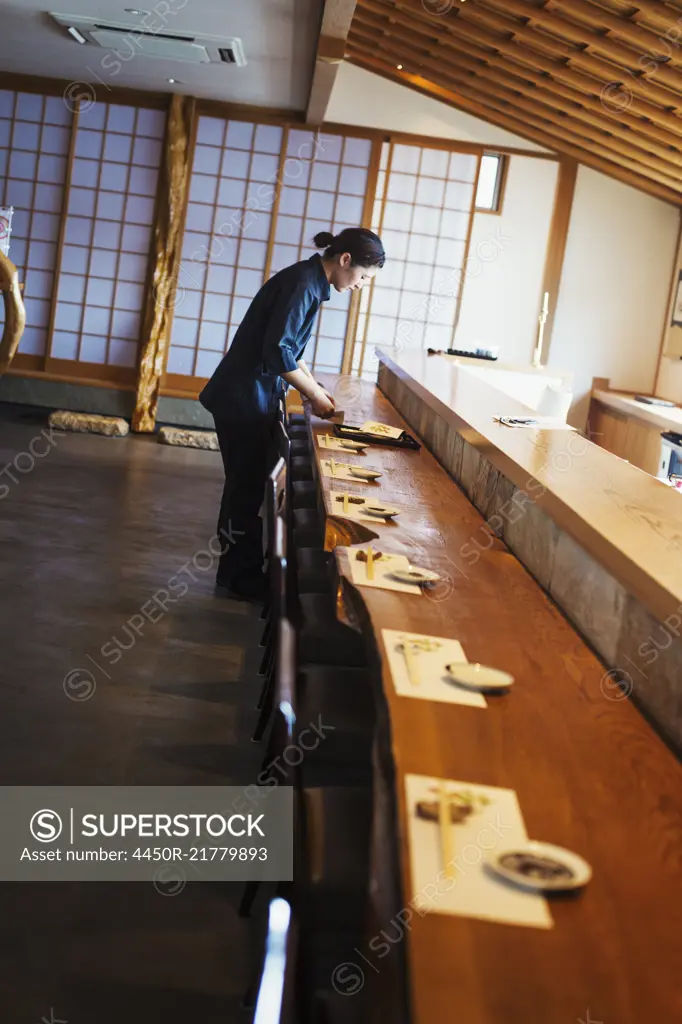 Waitress standing at a counter in a Japanese sushi restaurant, preparing place settings.