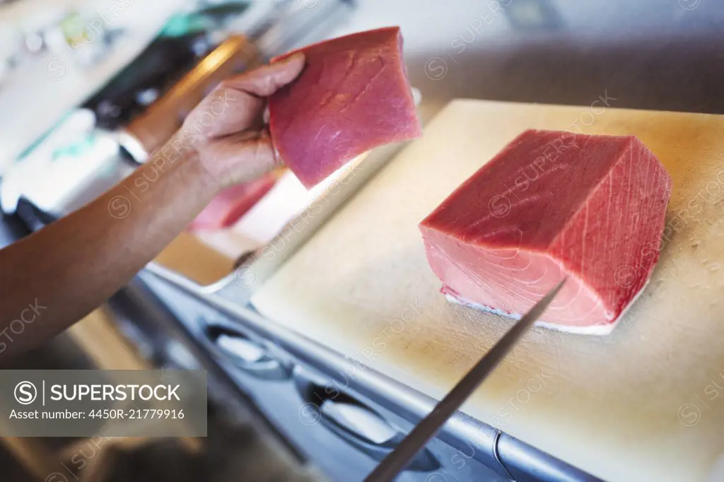 High angle close up of chef working at a counter at a Japanese sushi restaurant, slicing fillet of tuna.