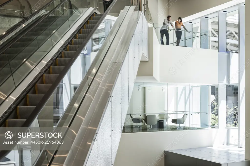 Businessman and woman at the top of an escalator in a large business centre.