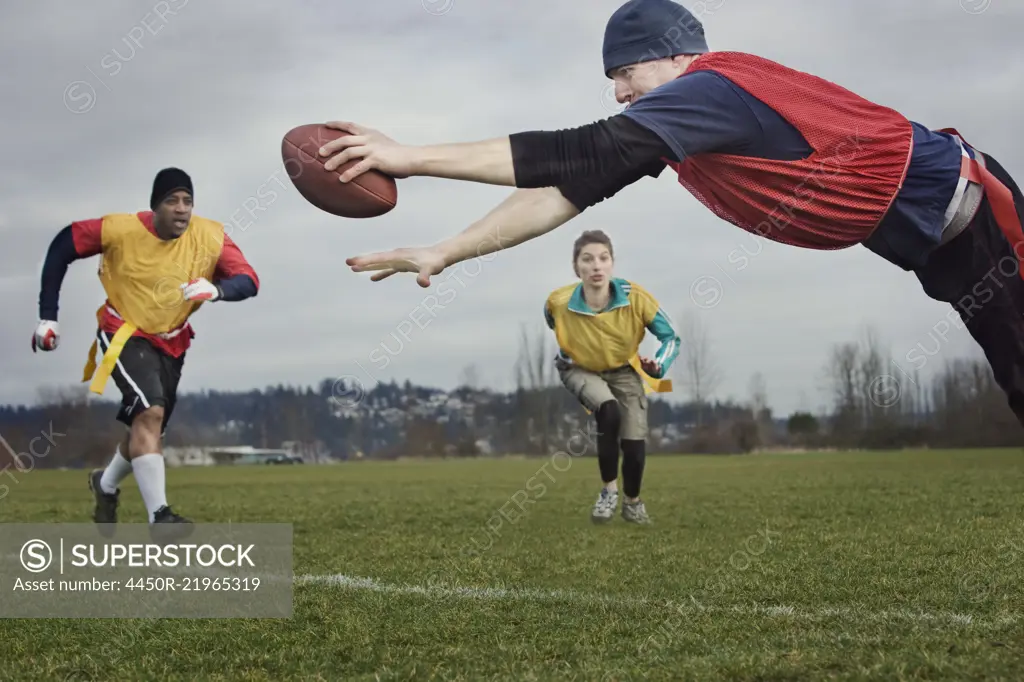 Caucasian man diving over the score line holding a football during an non-contact flag football match.