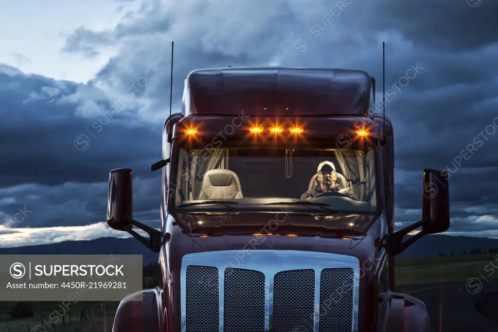 View into the cab of a  commercial truck with a driver in the front seat at night.