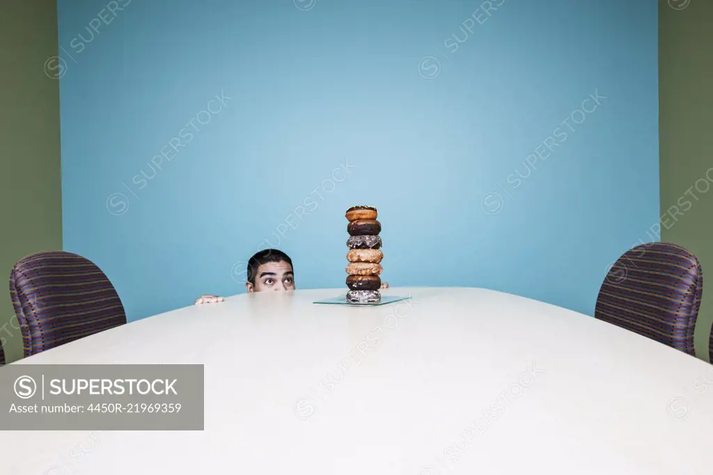 Businessman hiding behind a table with a stock of doughnuts on it.