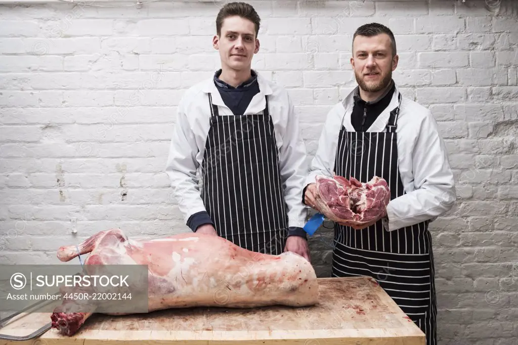 Two young men working, butchers jointing a whole lamb carcass.