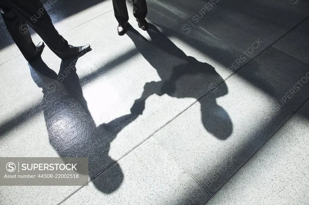A shadow on a tiled floor of two businessmen shaking hands.