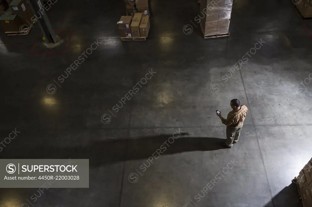 A storeroom manager seen from above in a darkened warehouse, looking at his phone.