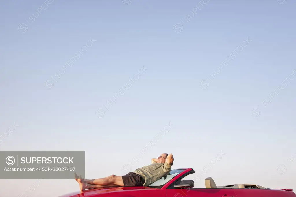 Caucasian male relaxing on the hood of his convertible sports car.