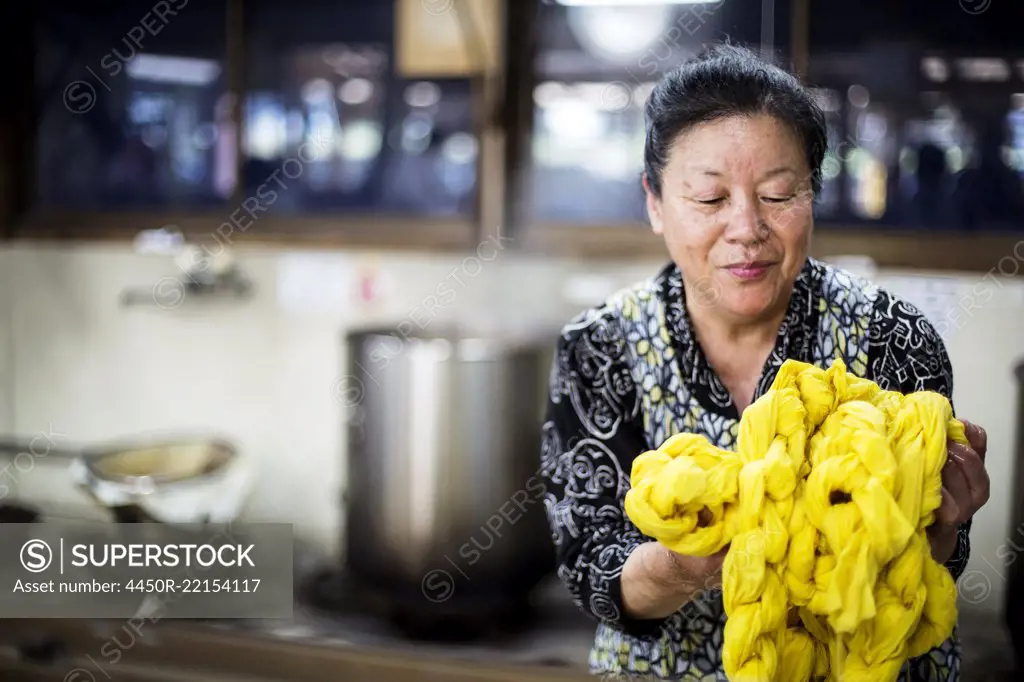 Japanese woman standing in a textile plant dye workshop, holding piece of bright yellow fabric.