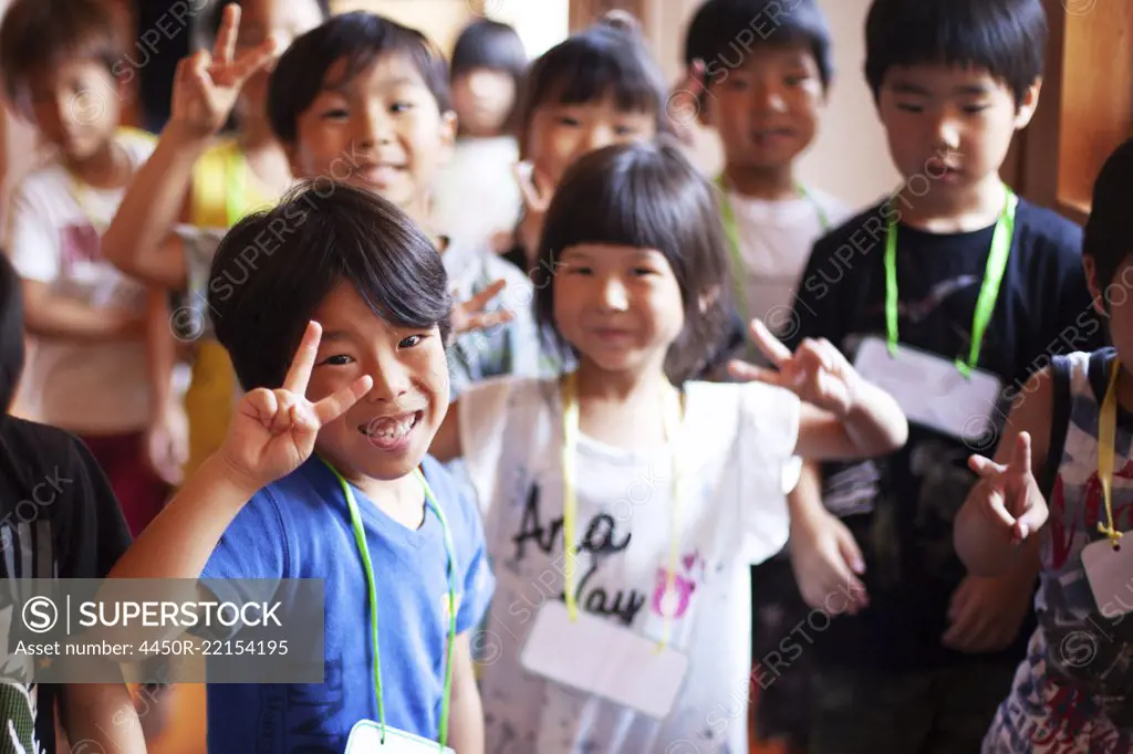 Group of smiling children in a Japanese preschool, making peace sign, looking at camera.