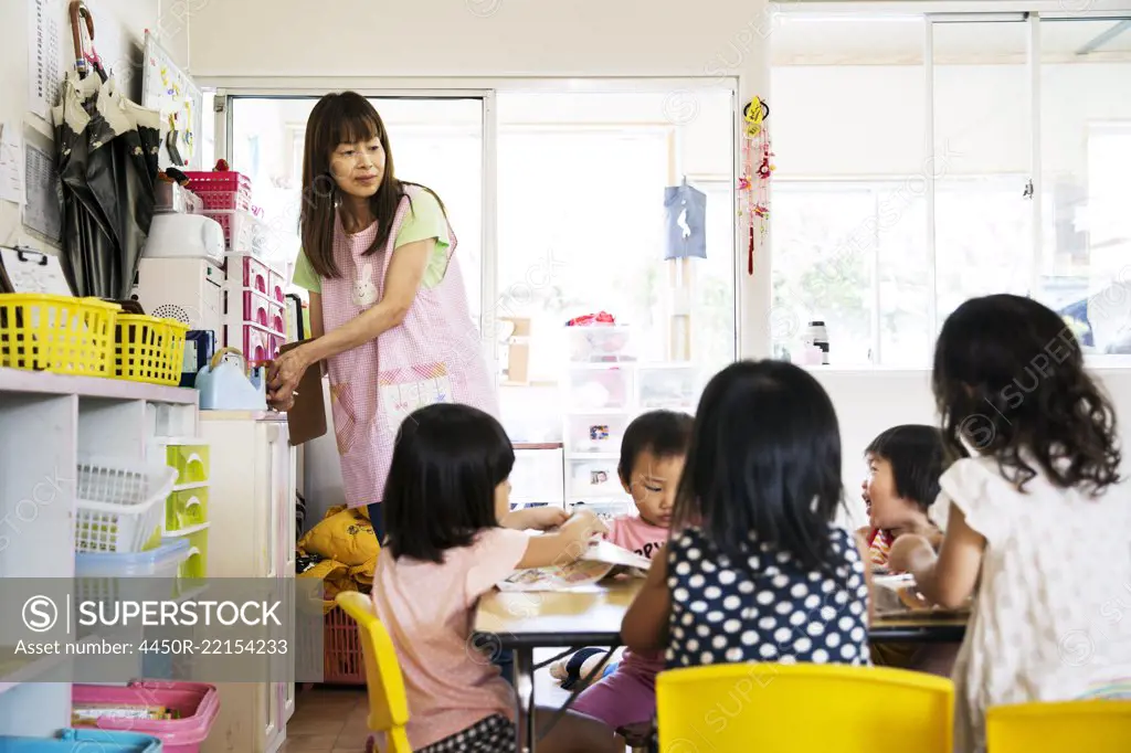 A young woman teacher and group of children in a Japanese preschool seated at a table. 