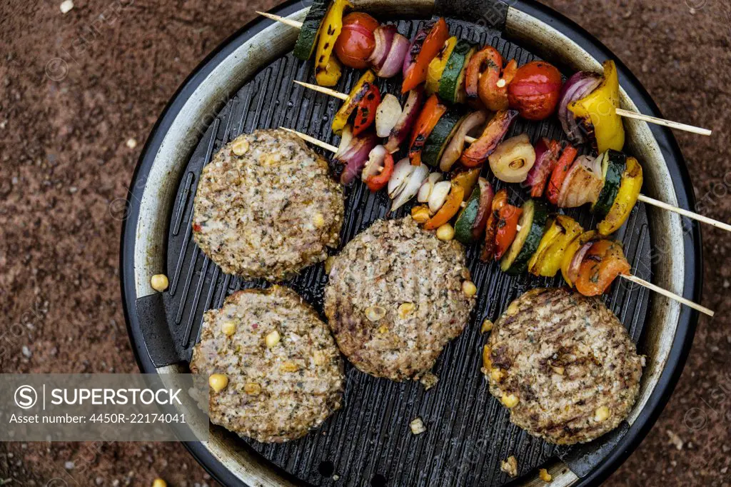 Food on a barbeque, vegetable kebabs and home made burgers, cooking outdoors.