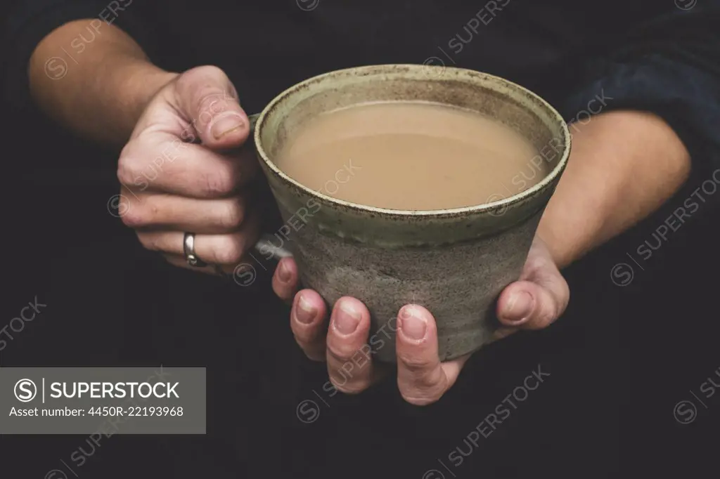 High angle close up of human hands holding green earthenware mug of tea.