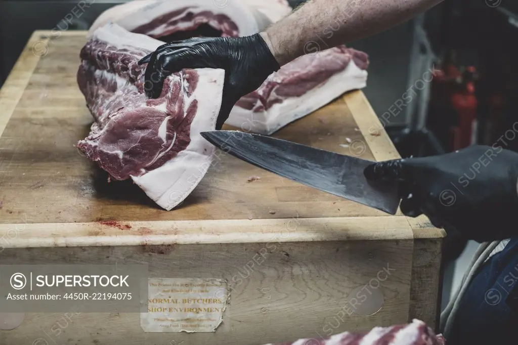 Close up of butcher wearing black rubber gloves cutting pork ribs on butcher's block.