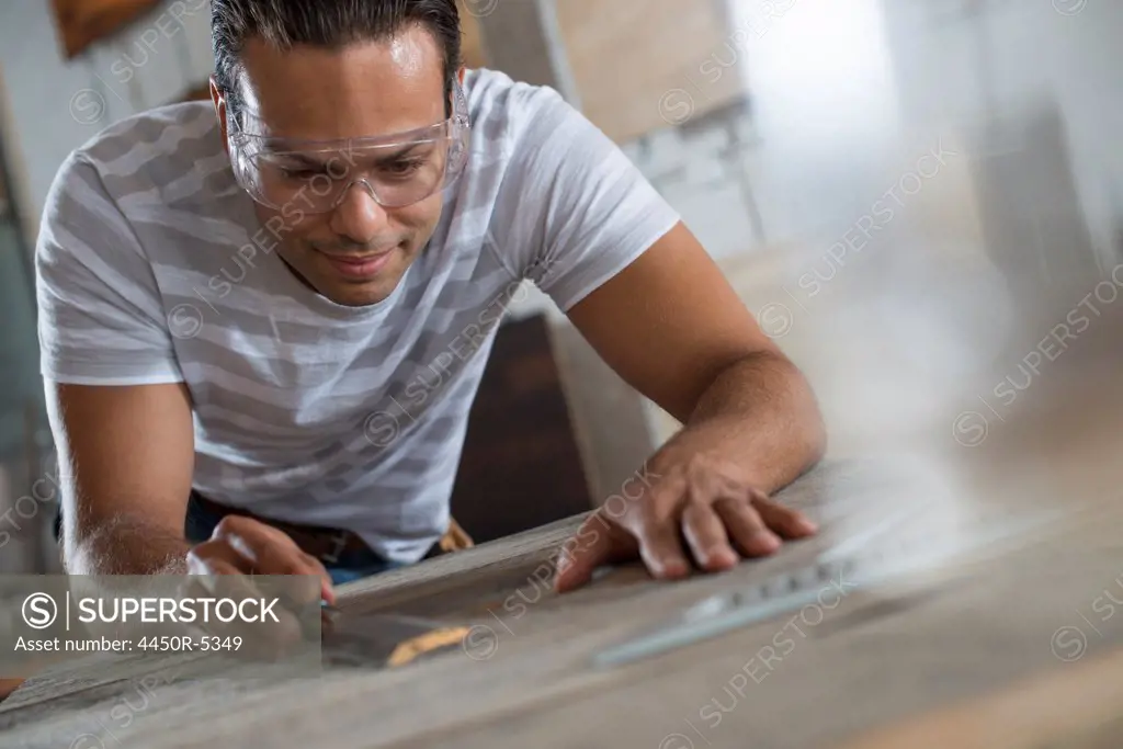 A young man in a workshop which uses recycled and reclaimed lumber to create furniture and objects. Measuring and drawing out plans on a counter top.
