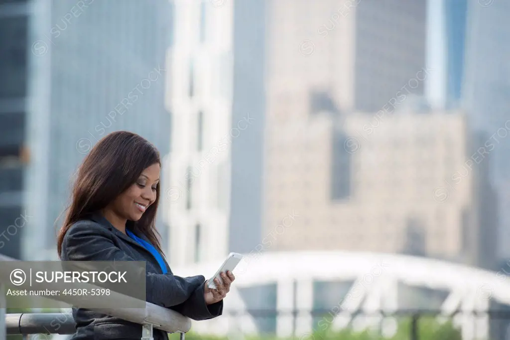 Summer in the city. Businesspeople outdoors, on the go. A woman in a grey suit using a smart phone.