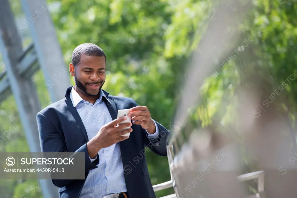 Summer in the city. Businesspeople outdoors, on the go. A man in a blue jacket and open necked shirt. Using a smart phone.