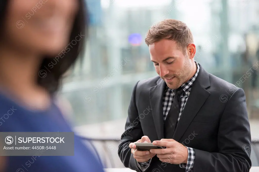 Business people out and about in the city. A man in a suit checking his phone. A woman in the foreground.
