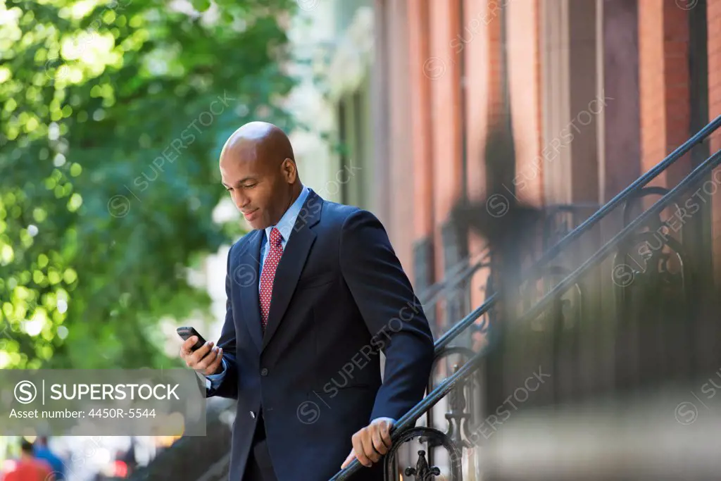 Business people outdoors, keeping in touch while on the go. A businessman in a suit and red tie, checking his phone.