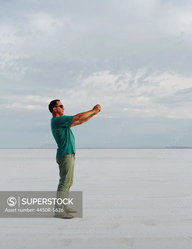 A man standing on Bonneville Salt Flats, taking a photograph with tablet device, at dusk.