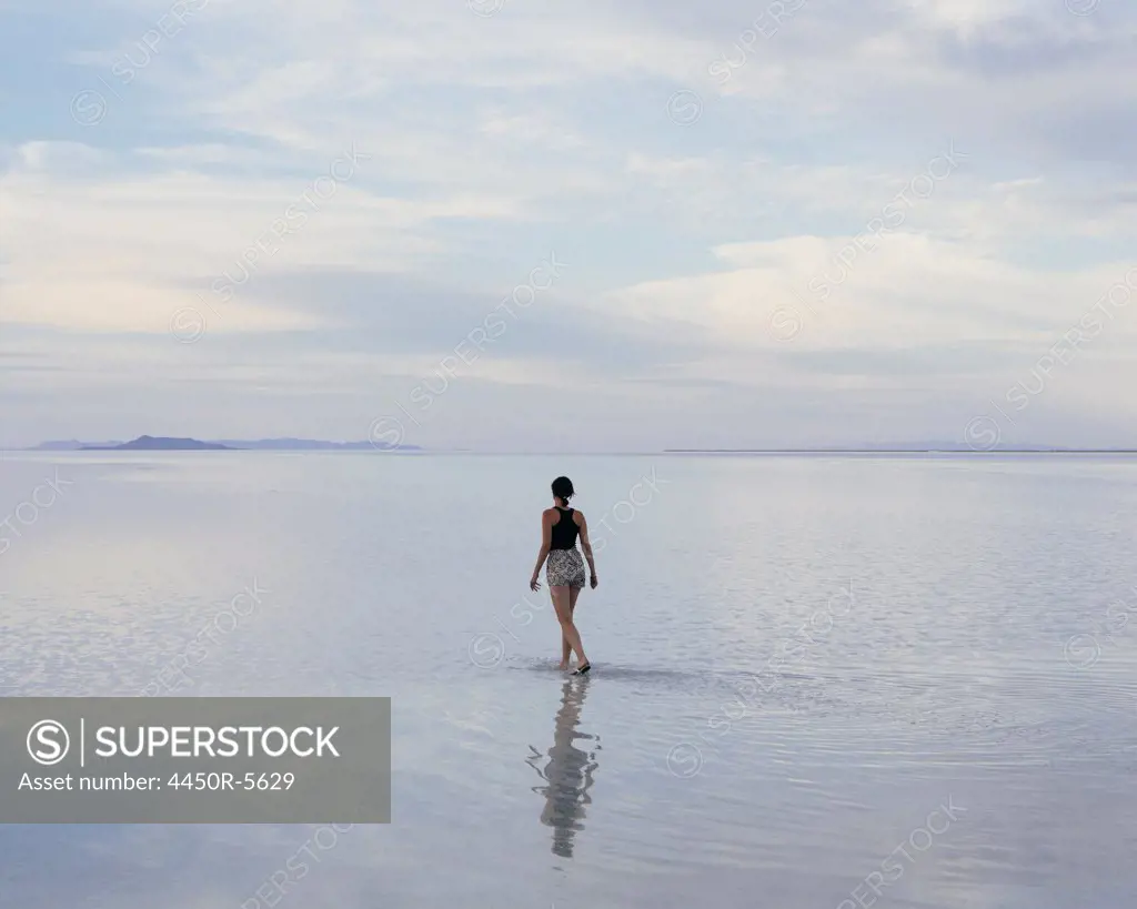 A woman standing on the flooded Bonneville Salt Flats at dusk. Reflections in the shallow water.