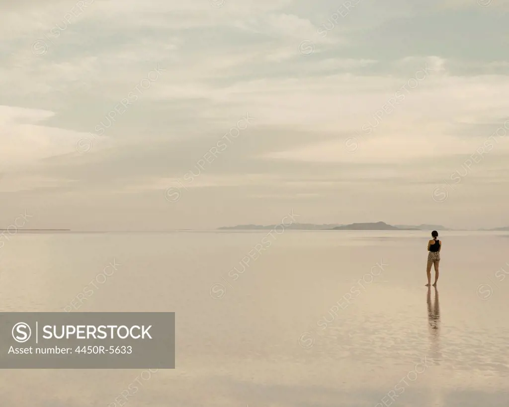 A woman standing on the flooded Bonneville Salt Flats at dusk. Reflections in the shallow water.
