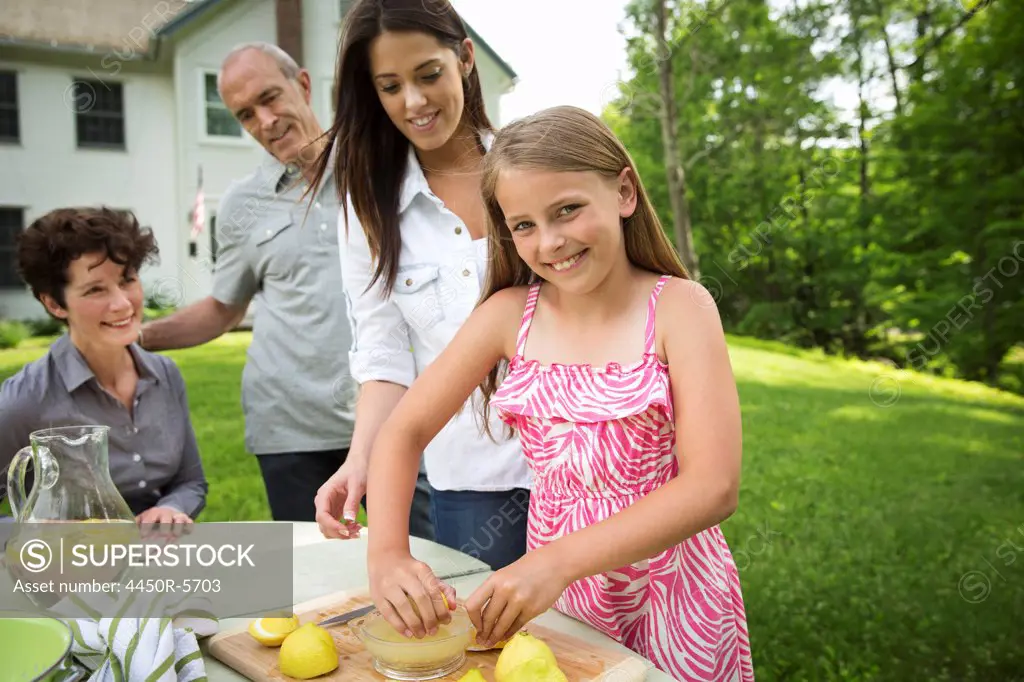 A summer family gathering at a farm. A girl slicing and juicing lemons to make lemonade.