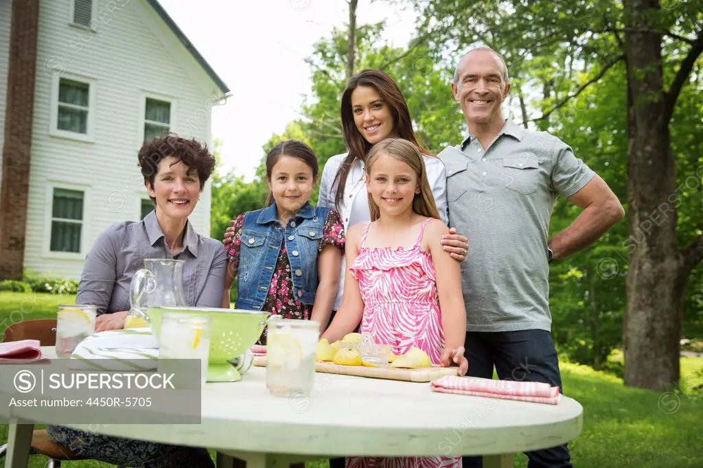 A summer family gathering at a farm. Five people posing beside the table, where a child is making fresh lemonade.