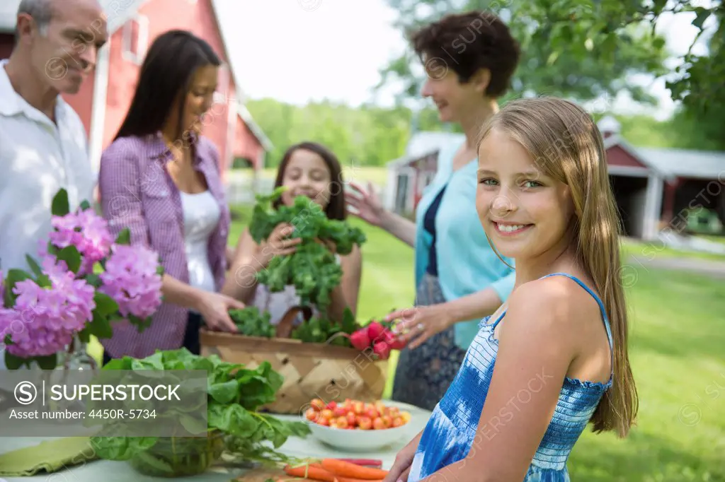 A summer family gathering at a farm. A table laid with salads and fresh fruits and vegetables. Parents and children.