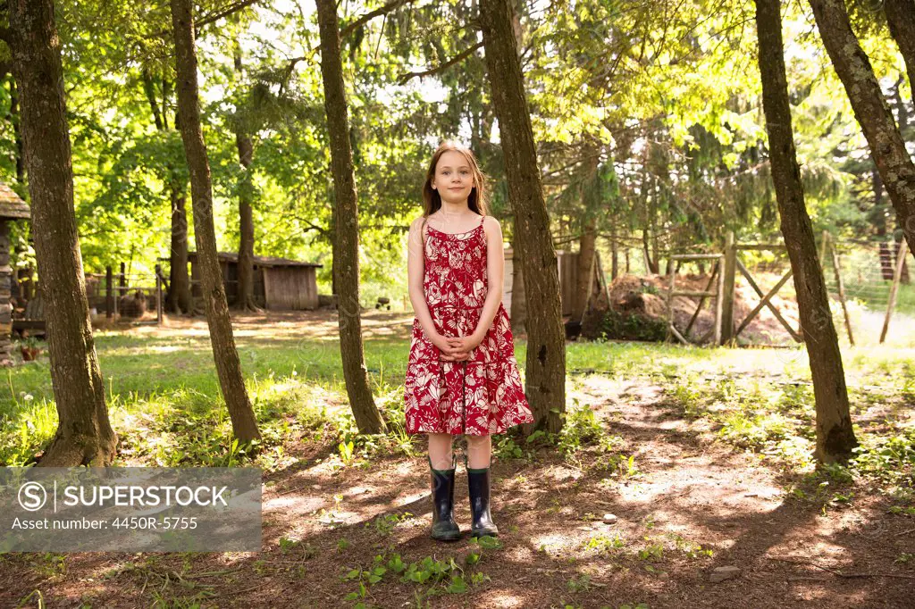 A girl in a summer dress standing in a grove of trees.
