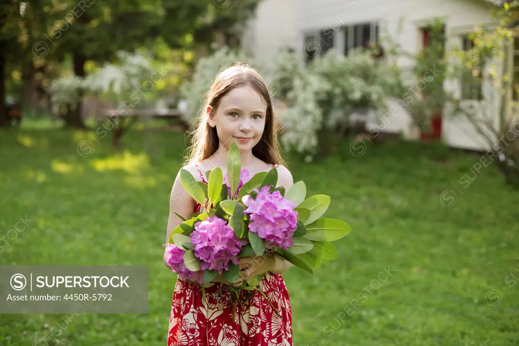 A young girl holding a bunch of purple rhododendron flowerheads.