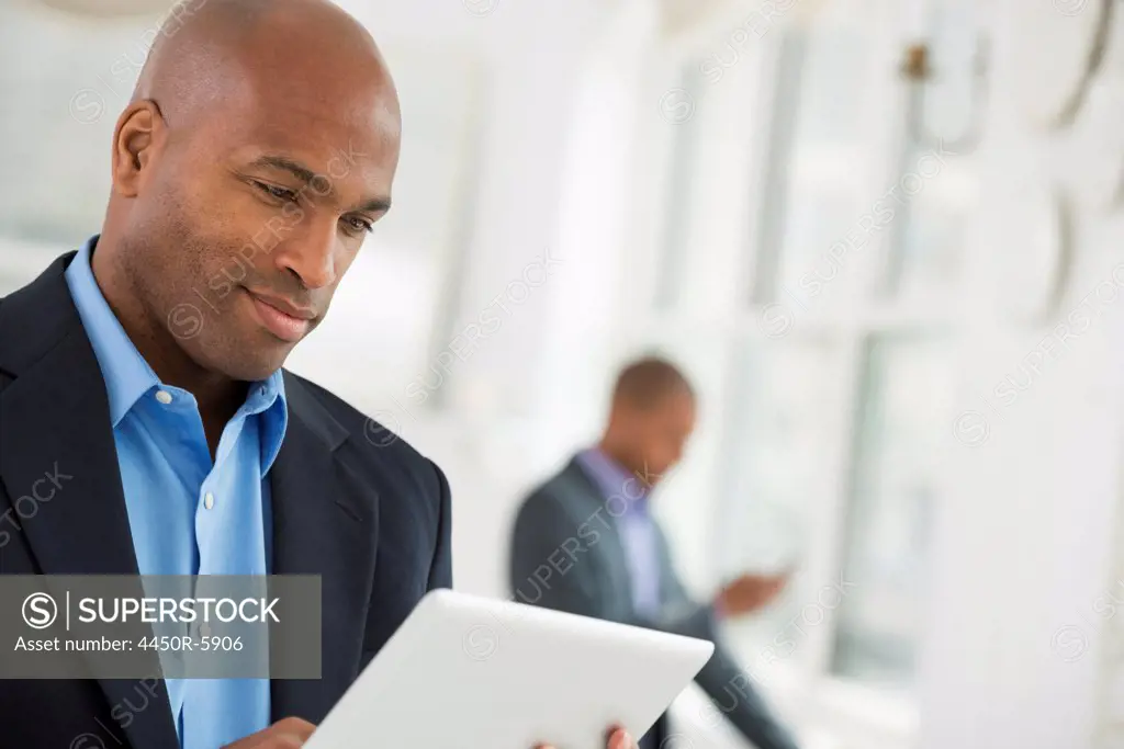 A business environment, a light airy city office. Business people. A man in a business suit using a digital tablet.