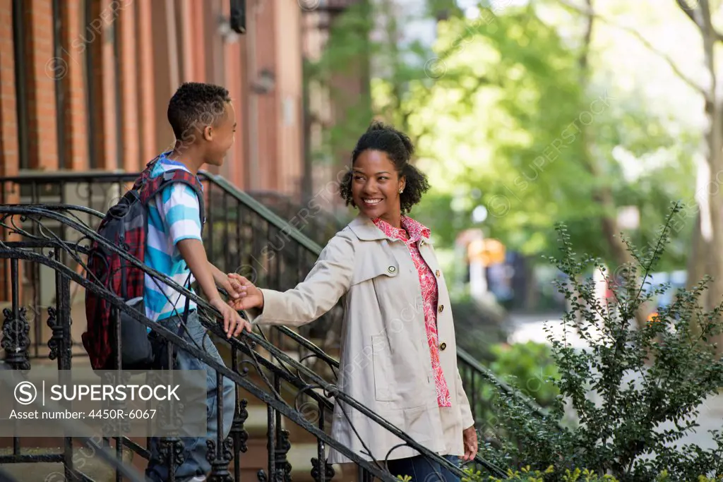 A mother and son, a woman and a boy on a flight of steps outside a brownstone building.