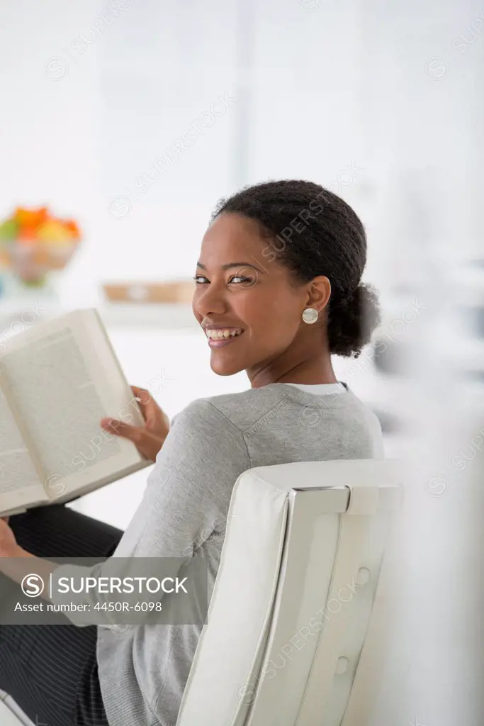 An office in the city. Business. A woman sitting and reading a book. Research or relaxation. Looking over her shoulder and smiling.