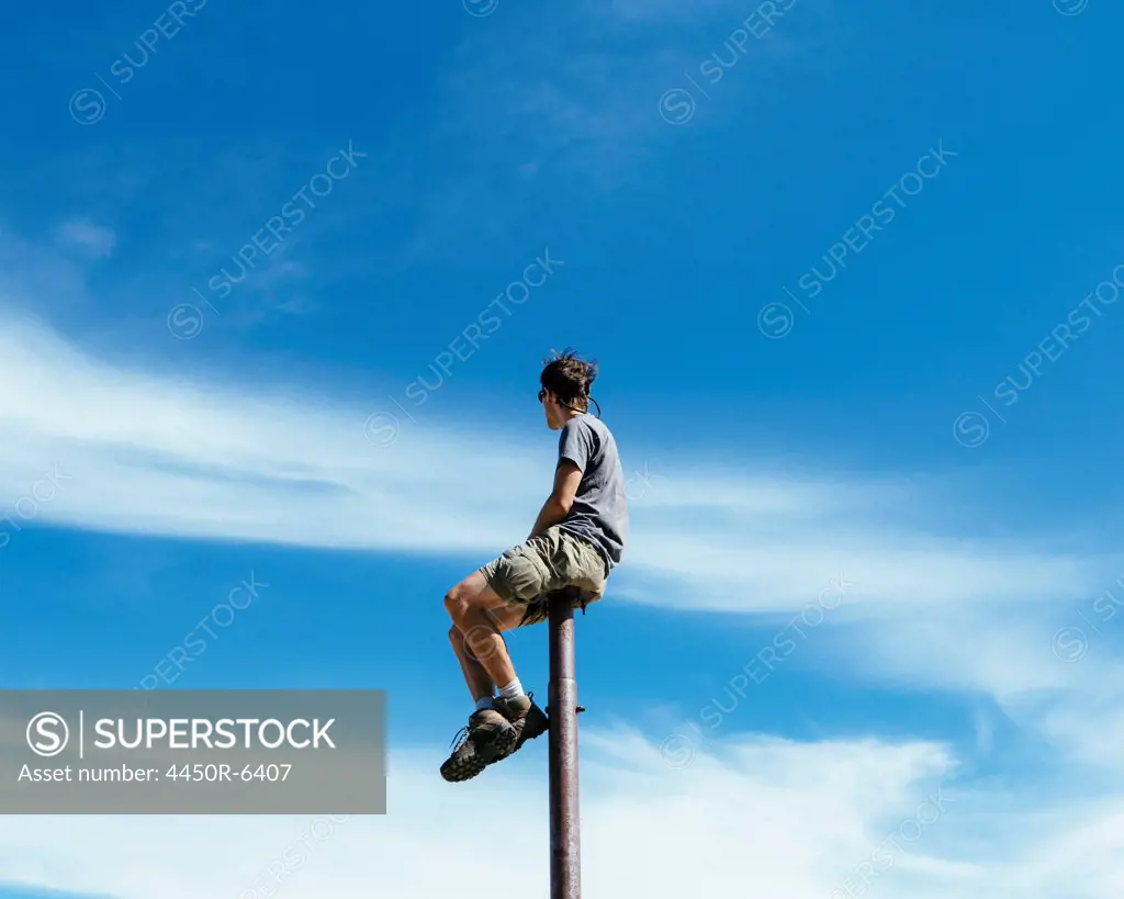 Man sitting and balancing on top of a metal post, looking towards expansive sky, on Surprise Mountain, Alpine Lakes Wilderness, Mt. Baker-Snoqualmie national forest.