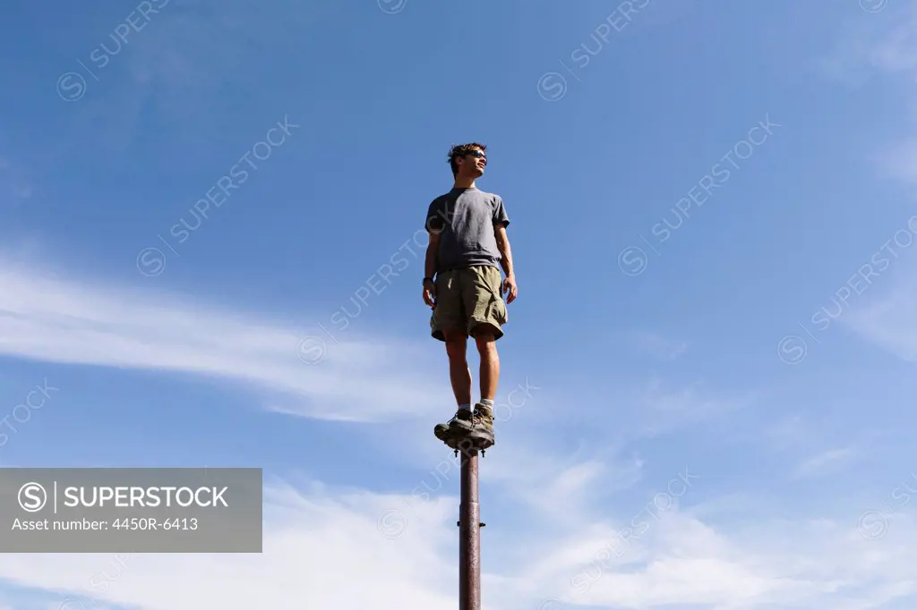 Man standing and balancing on a metal post, looking towards expansive sky, Surprise Mountain, Alpine Lakes Wilderness, Mt. Baker-Snoqualmie National forest.
