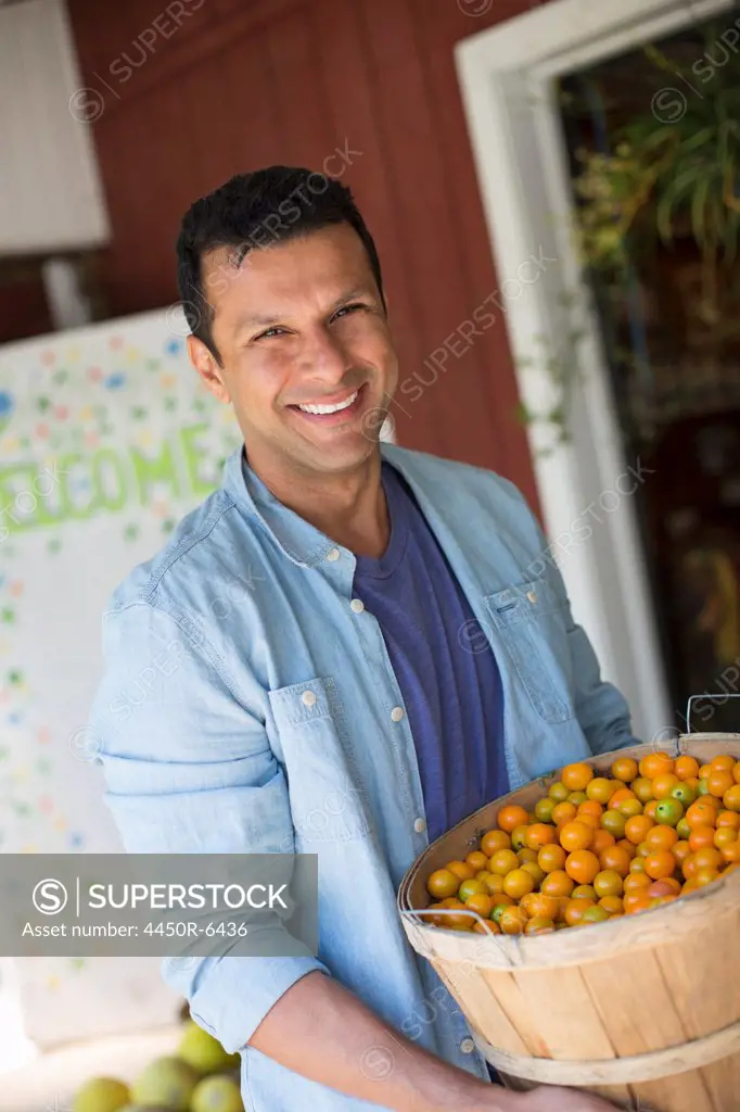 A farm growing and selling organic vegetables and fruit. A man holding a bowl of basket of freshly picked tomatoes.