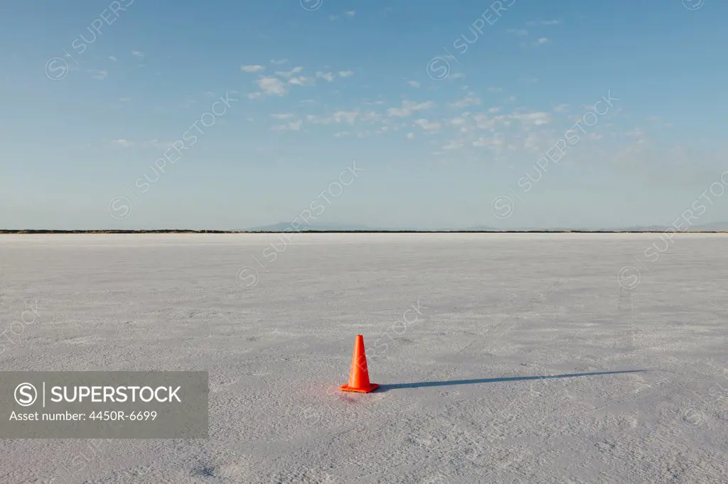 A solitary traffic cone on the white reflective mineral dusted surface of the Bonneville Salt Flats in the early morning light.