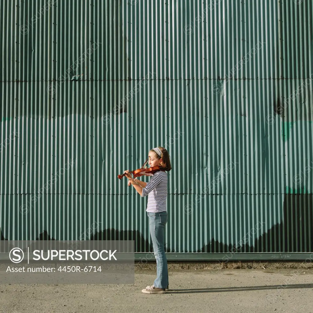 A ten year old girl playing the violin on an urban street.