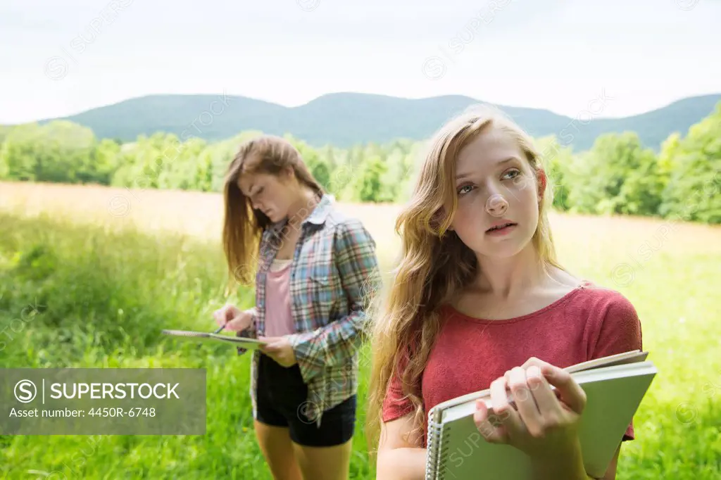 Two young girls sitting outside on the grass, with sketch pads and pencils.