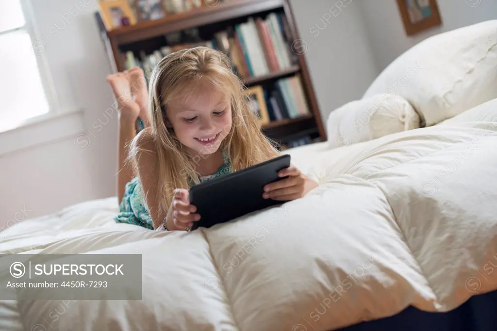 A young girl sitting on her bed using a digital tablet.