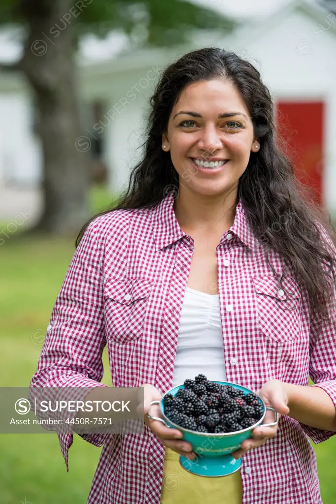 A woman holding a bowl of freshly picked blackberries.
