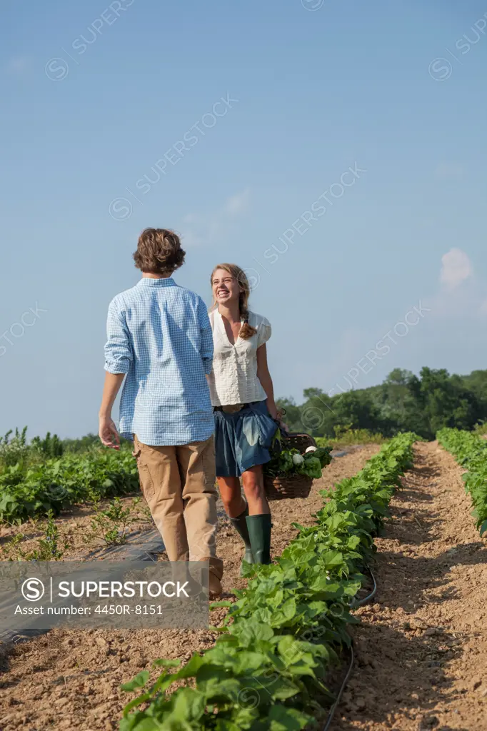 A girl leading a boy by the hand in a field of growing produce and vegetable plants. Maryland, USA. 7/1/2012