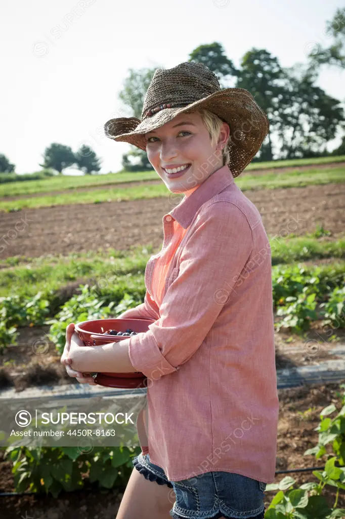 A girl in a pink shirt holding a large bowl of harvested blueberry fruits. Maryland, USA. 7/1/2012