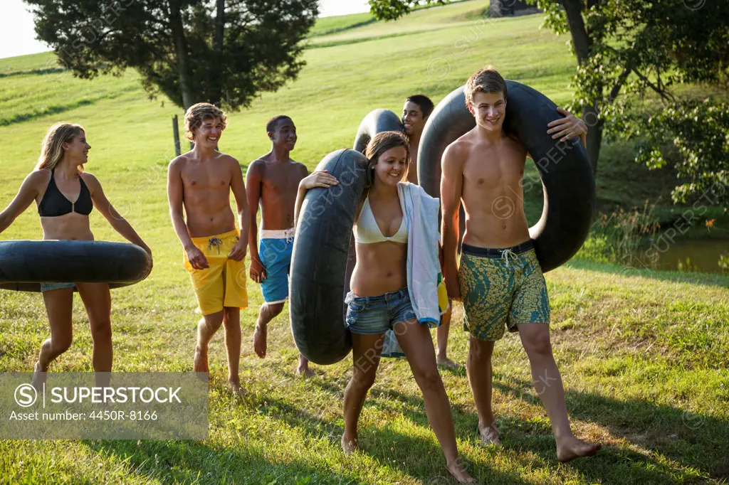 A group of young people, boys and girls, holding towels and swim floats, going for a swim. Maryland, USA. 7/1/2012