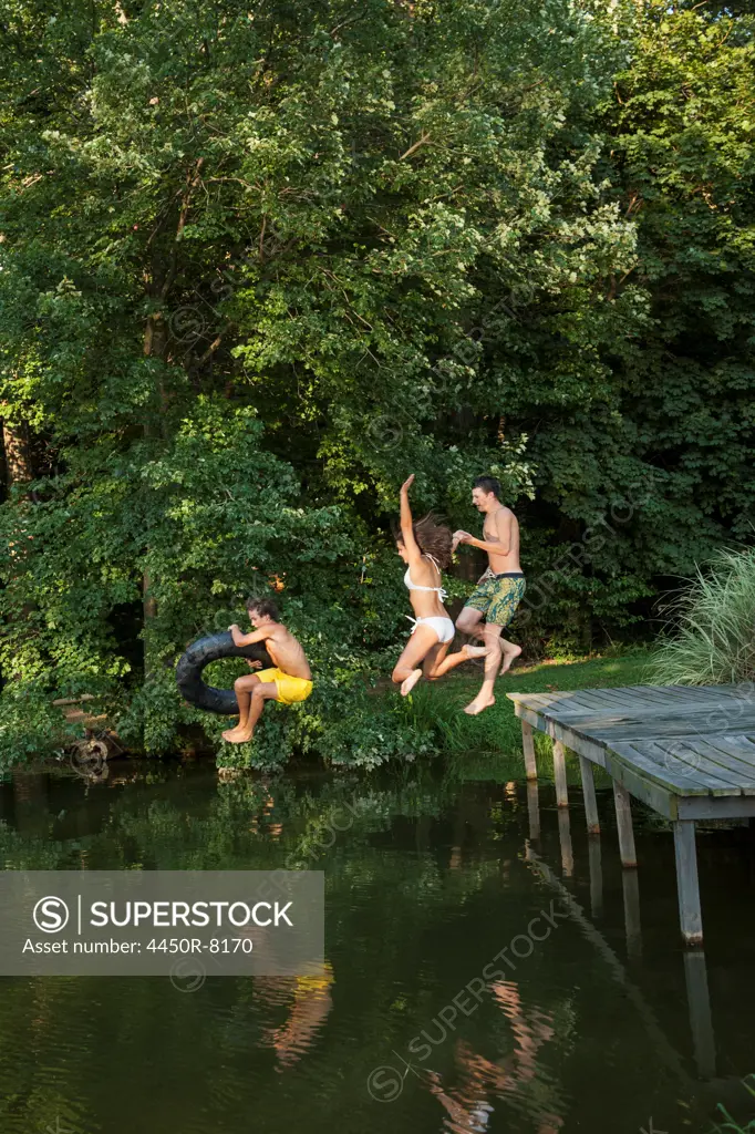 Three young boys jumping from the jetty into a still pool of water. Maryland, USA. 7/1/2012