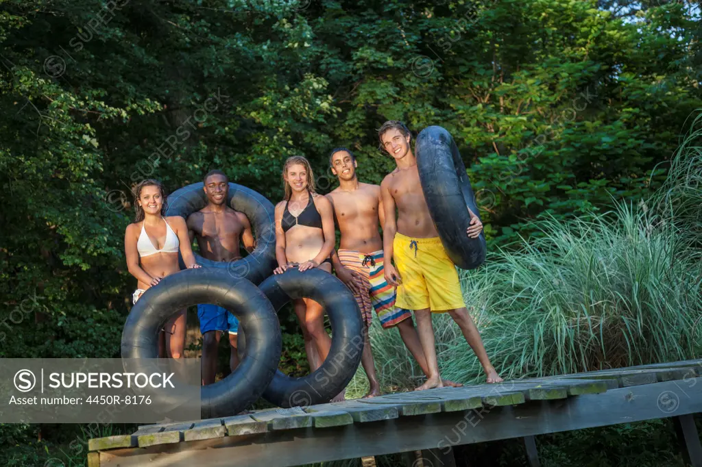 A row of five young people with swim floats on the jetty by a natural pool. Maryland, USA. 7/1/2012
