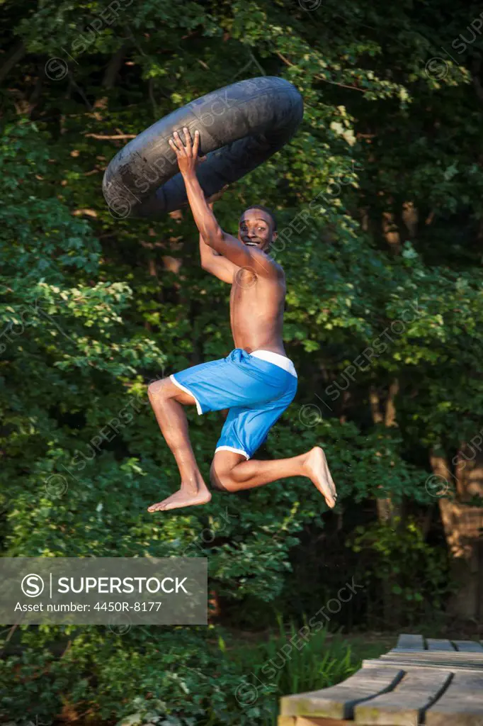 A young person, boy holding a swim float tyre over his head and leaping into the water from the jetty. Maryland, USA. 7/1/2012